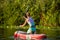 Young athletic woman doing fitness on a board with an oar on a lake.