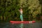 Young athletic woman doing fitness on a board with an oar on a lake.