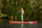 Young athletic woman doing fitness on a board with an oar on a lake.