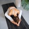 Young athletic woman practicing yoga doing variation of kurmasana exercise, turtle pose, exercising alone while sitting on mat in