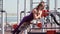 Young athletic woman in a sports purple tracksuit does lumbar hyperextension exercise on workout ground in a city park.