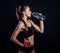 Young athletic woman in sportswear drinking water in studio against black background. Ideal female sports figure.