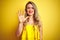 Young attactive woman wearing t-shirt standing over yellow isolated background showing and pointing up with fingers number five