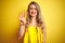 Young attactive woman wearing t-shirt standing over yellow isolated background showing and pointing up with fingers number four