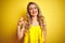 Young attactive woman wearing t-shirt standing over yellow isolated background smiling and confident gesturing with hand doing