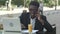 Young attractive afro american businessman with glasses and laptop sitting in cafe bar and talking on cell phone