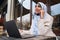 Young attractive Arabic businesswoman in hijab talking on smartphone during work on laptop on street