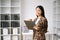 Young attractive Asian female office worker business suits smiling at camera with working notepad, tablet and laptop documents .