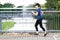 Young attractive asian runner woman running at sidewalk way in public nature city park with lake water view wearing blue or black