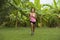 Young attractive Asian sport runner woman running in the jungle smiling happy in training workout on herb with palm trees on the b