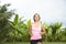 Young attractive Asian sport runner woman running in the jungle smiling happy in training workout on herb with palm trees on the b