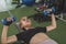 A young and attractive asian woman does bench presses with a pair of blue rubberized dumbbells. Working out chest and upper body