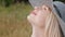 A young attractive blond woman in a blue dress and hat is sitting on a plaid on the grass. The wind blows hair.