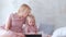 Young attractive blond woman with her little charming daughter in pink dresses seriosly watching something in tablet.