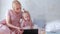 Young attractive blond woman with her little charming daughter in pink dresses watching video in tablet.