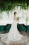 Young attractive bride in wedding dress with bridal veil looks at bouquet and smiles. Girl in wedding gown in modern