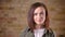 Young attractive brown-headed woman turns to camera and smiles on bricken wall background.