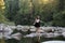 Young attractive brunette woman on a rock next to a pristine river in an evergreen forest.