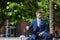 Young and attractive businessman, with beard and suit, sitting on a bench next to his suitcase waiting for a cab. Concept beauty,