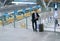 Young attractive businessman standing with his rolling suitcase inside the airport, leaning at the glass guard railing