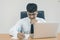 Young attractive businessman thinking, writing on paper and computer laptop at office.