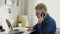 Young attractive businessman wearing glasses with yellow hair working at home. Talking on the phone sitting at the desk