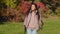 Young attractive carefree woman hiker travels with backpack trekking sticks walking outdoors in autumn park admiring