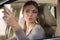 Young attractive caucasian woman behind the wheel driving a car, smiling and making selfie on mobile phone.