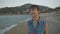 Young attractive caucasian woman in plaid blue shirt walking on pebble beach along the sea.