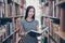 Young attractive clever successful asian female student is holding big thesaurus in hard bookcase, wearing casual striped t shirt