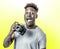 Young attractive and cool happy black afro American man holding digital reflex photo camera smiling excited on yellow bac