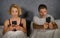 Young attractive couple using mobile phone in bed ignoring and neglecting each other obsessed networking in internet addiction and