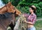 Young attractive cowgirl feeding horses in the farm