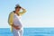 Young attractive european pregnant woman in yelow shirt and white hat is staying at the shore of tranquil blue sea and holding tum