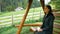 Young attractive farmer woman drinking coffee while sitting on a wooden swing.A young attractive woman is drinking