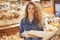 Young attractive female model with appealing appearance stands in bakery department, chooses bread or buns, spends free time in gr