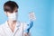 A young attractive female scientist in a mask holds a package of pills with gloved fingers on blue background