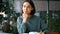 Young attractive female student reads a book and ponders what she has read while sitting at a table in a public library