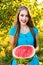 Young attractive girl holding half of ripe watermelon