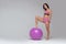 Young attractive girl in modern pink sportswear is posing putting her foot on fitness ball  on grey background