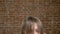 Young attractive girl moves her head, plays her hair, brick background