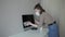 A young attractive girl in a quarantine protective mask thoroughly cleans the computer with a disinfectant.Coronavirus