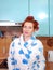 The young attractive girl with red hair in a dressing gown and with wound hair curlers costs in kitchen and smiles.