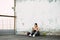 A young attractive girl in sportswear on the Playground sits on the asphalt near the wall and uses her smatrphone in the summer at