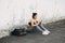 A young attractive girl in sportswear on the Playground sits on the asphalt near the wall and uses her smatrphone in the summer at