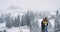 Young attractive guy and lady standing on the top of field background amazing snowy forest , they looking at the