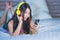 Young attractive and happy Asian Chinese woman with yellow headphones listening to music in mobile phone on bed at home smiling ha