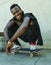 Young attractive and happy black afro American man squatting on skate board smiling at grunge street corner looking cool posing in