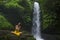 Young attractive and happy hipster woman enjoying nature feeling free outdoors at amazing beautiful waterfall in exotic holidays