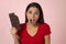 Young attractive and happy hispanic woman in red top smiling excited eating chocolate bar on pink background